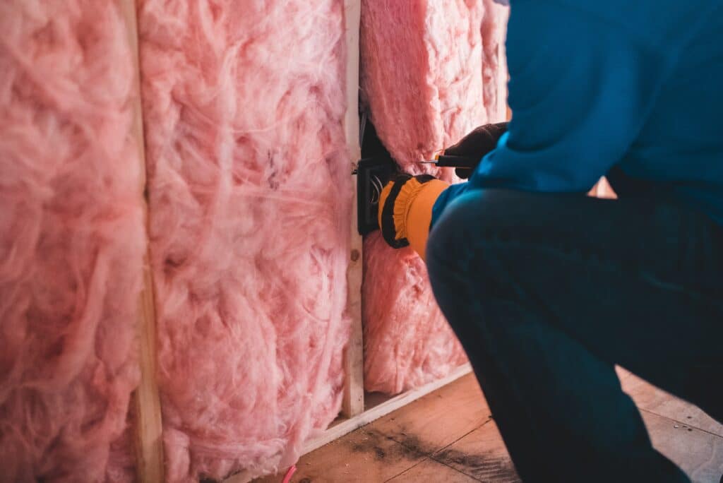 A man properly installing insulation in a wall.