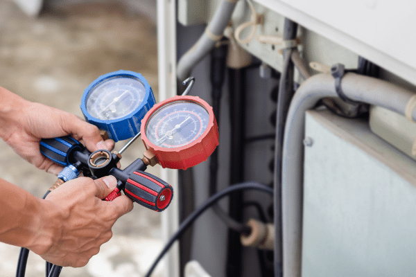 Hands of HVAC technician reading red and blue gauge of a residential AC unit 